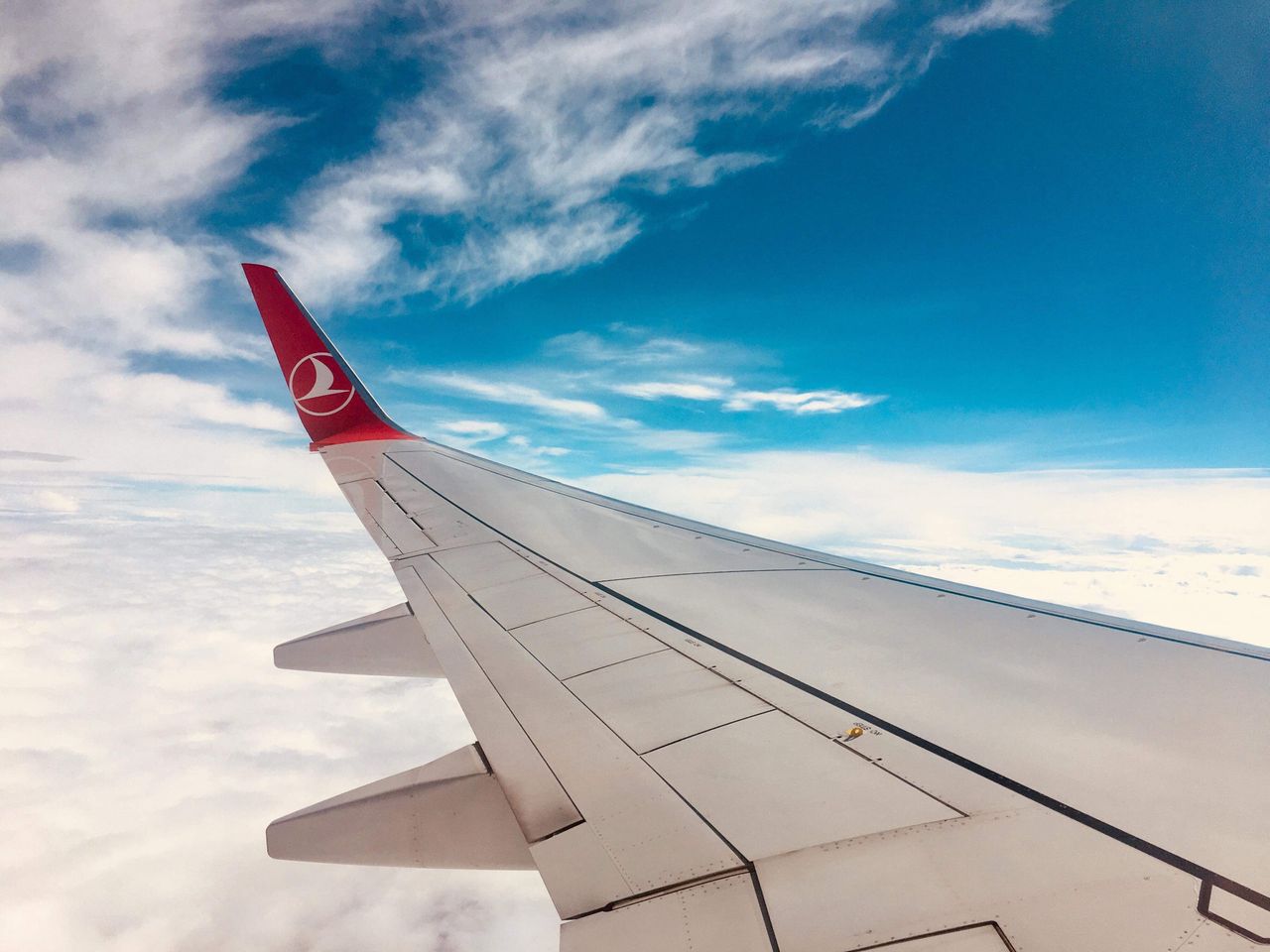 Photo of an airplane wing against a vivid blue sky and soft clouds.
