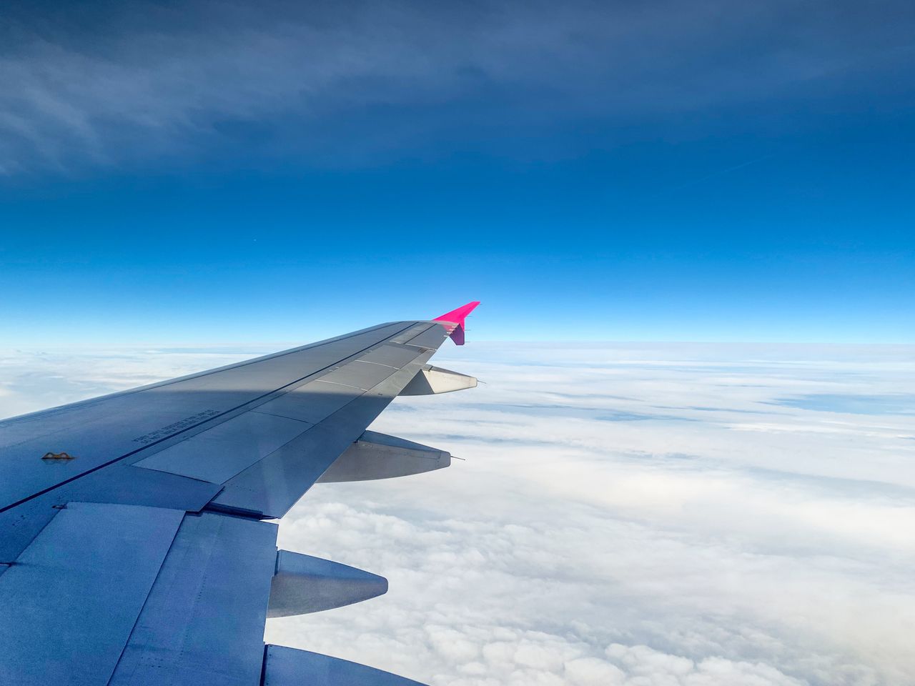 Services Aerial view of an airplane wing above clouds with clear blue sky, offering serene travel vibes.